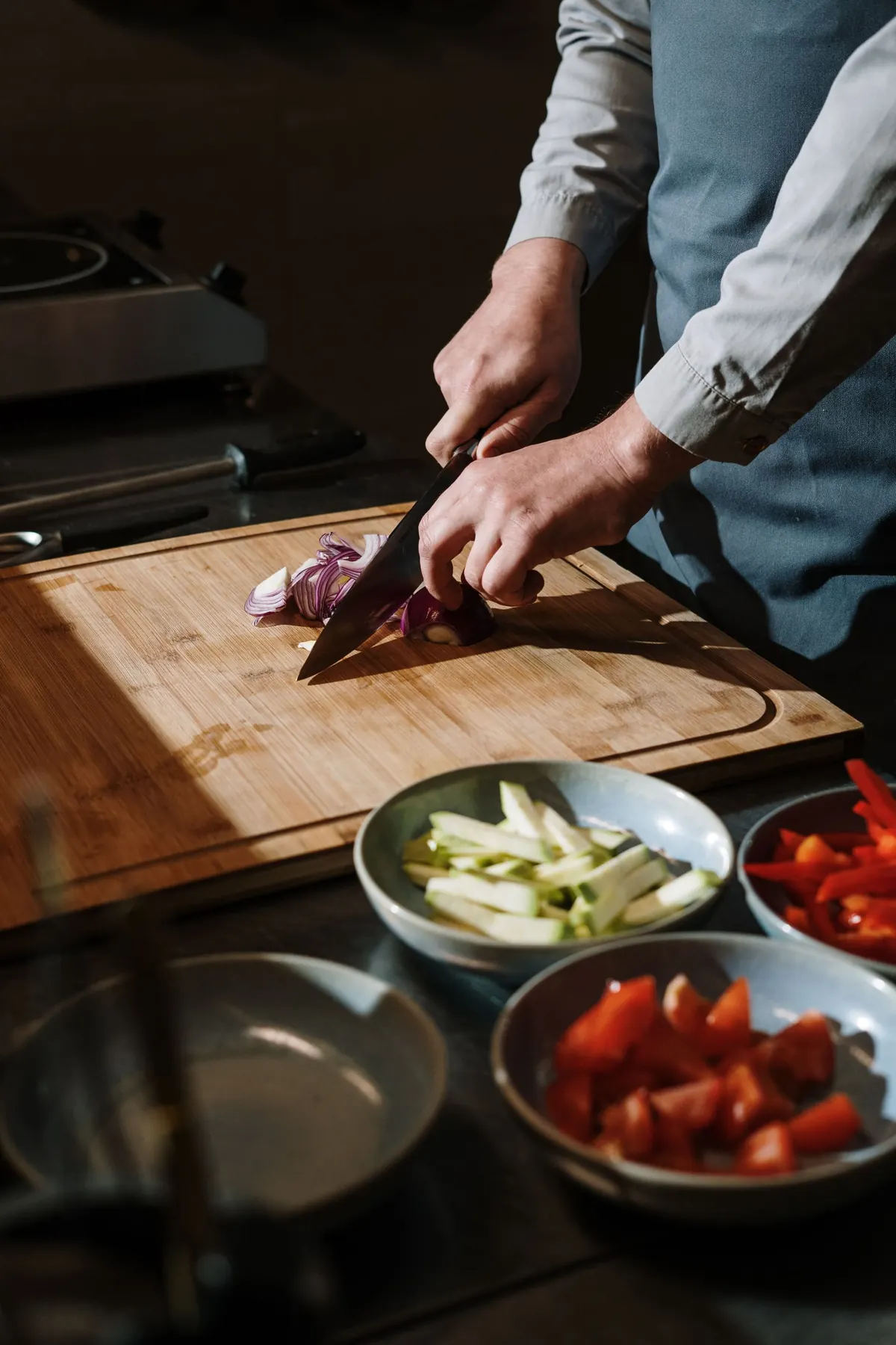 Cuisinier &eacute;min&ccedil;ant des oignons sur une planche en bois, l&eacute;gumes pr&eacute;par&eacute;s en bacs