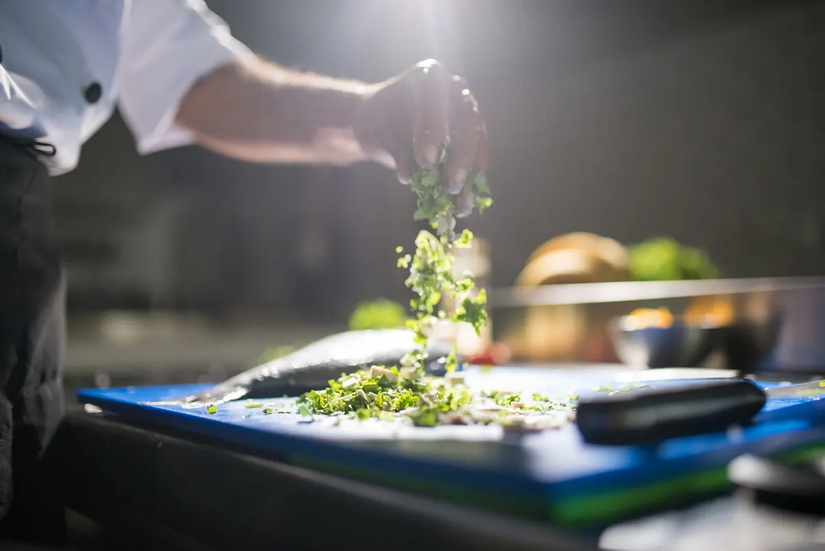 Mains d&rsquo;un cuisinier disposant des herbes fra&icirc;ches sur une planche en cuisine professionnelle